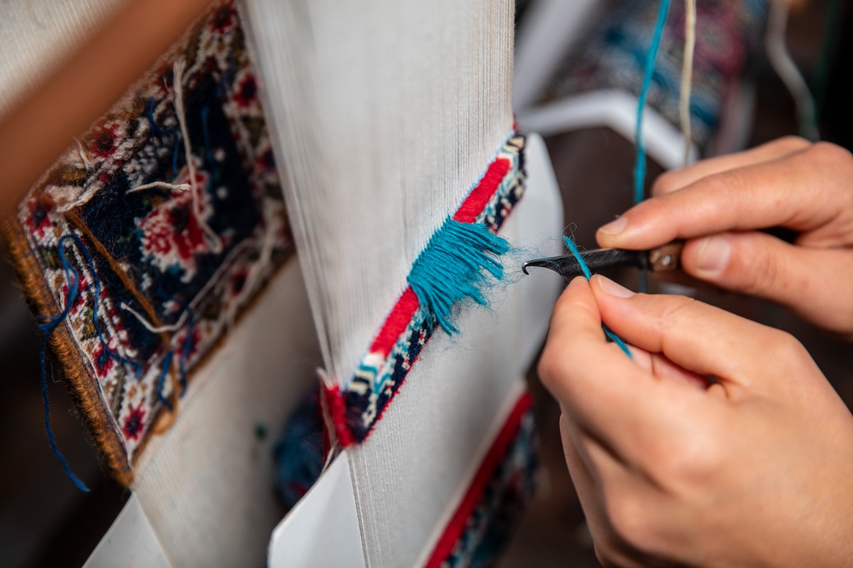 A skilled artisan meticulously re-weaving the fibers of an antique Persian carpet, showcasing expert oriental rug repair near me at Rose Oriental Rugs in Berkeley.