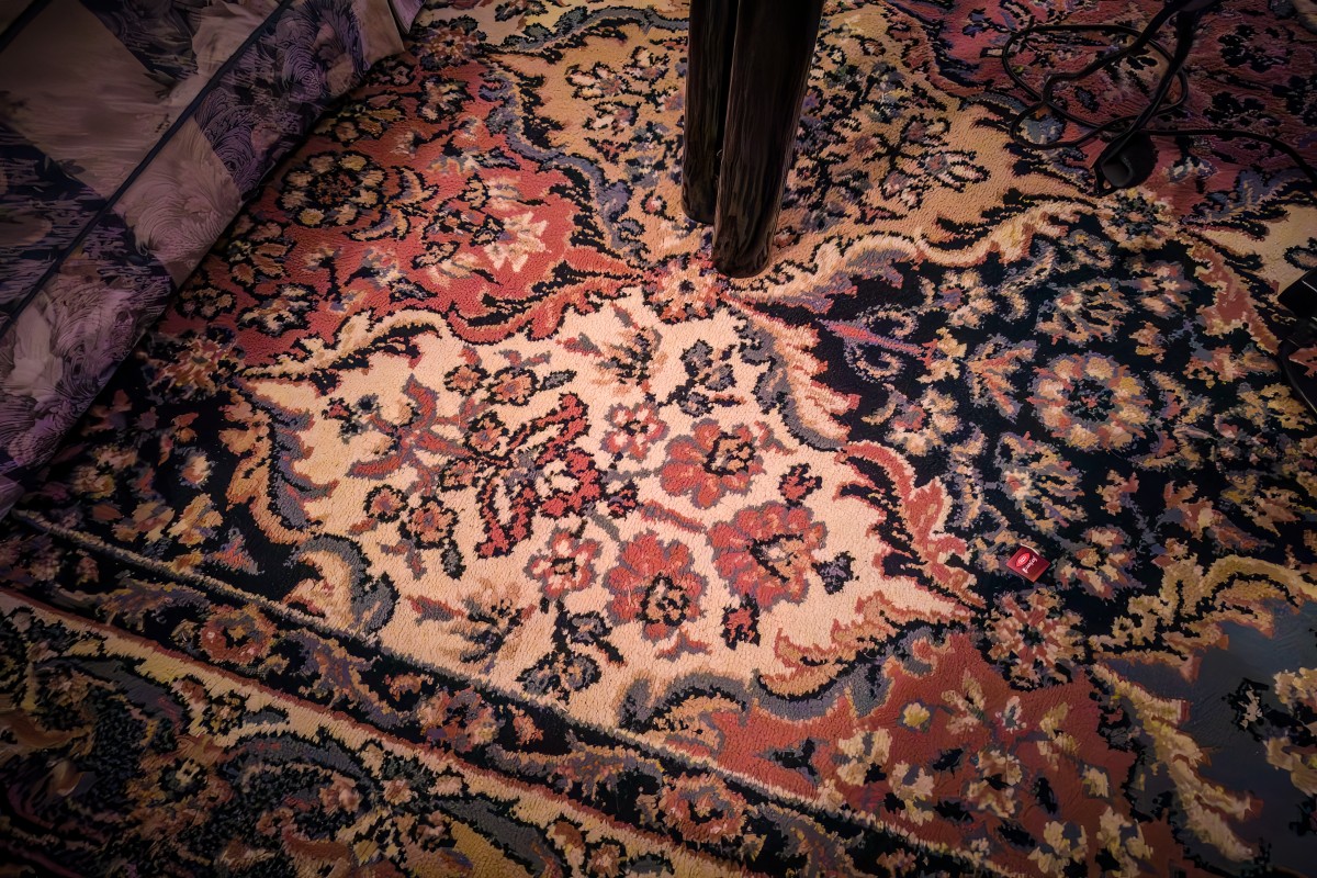 Textile conservator inspecting the fine knots and fringe of an authentic Persian antique wool and silk rug during maintenance.